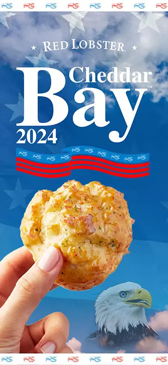 A hand holding a cheddar bay biscuit over a background of clouds, the United States flag, and an eagle